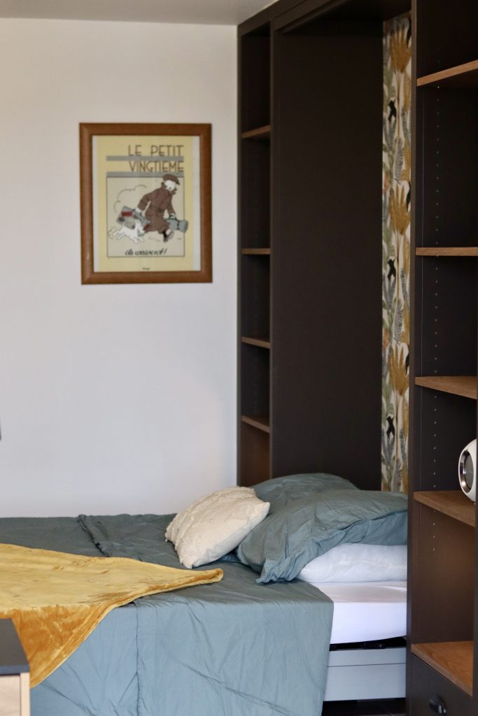 Projet Charlie - chambre avec étagère en bois, lit et lampe, papier peint fleuri